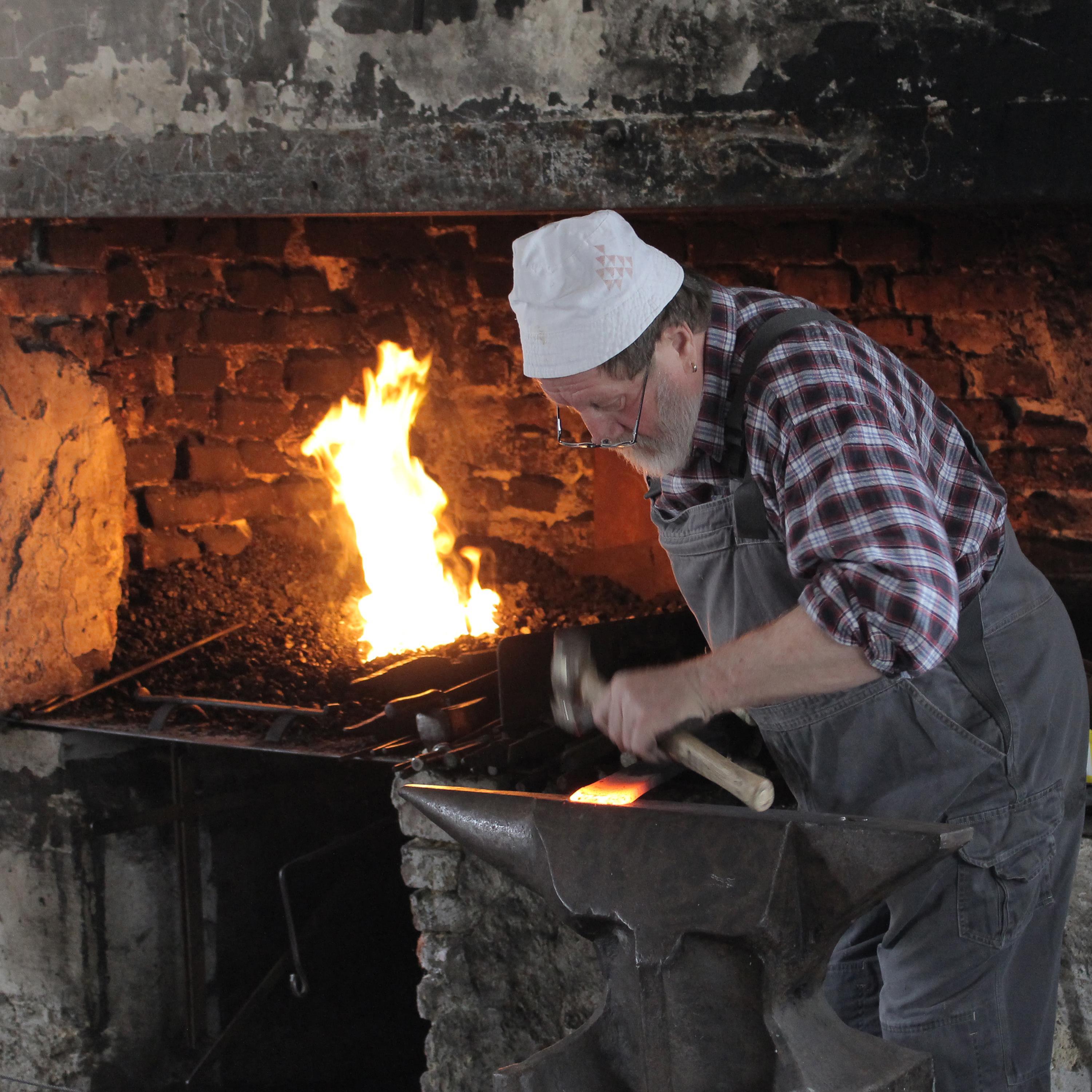 Schmied mit Hammer und Werkstück neben offenem Feuer