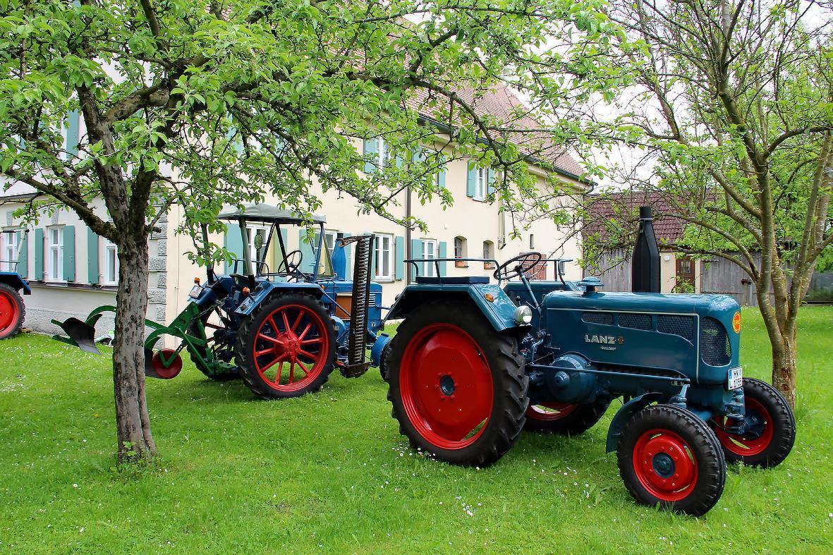 Historischer Traktor unter Apfelbäumen, dahinter der Stockerhof
